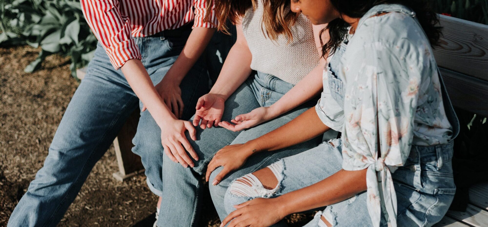 Three people sitting together. Two people have their hands on the knee of a person in the middle. 